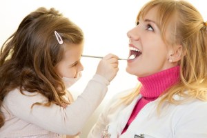 Young girl pretending to be a dentist while examining a smiling female dentist's mouth with a dental mirror tool